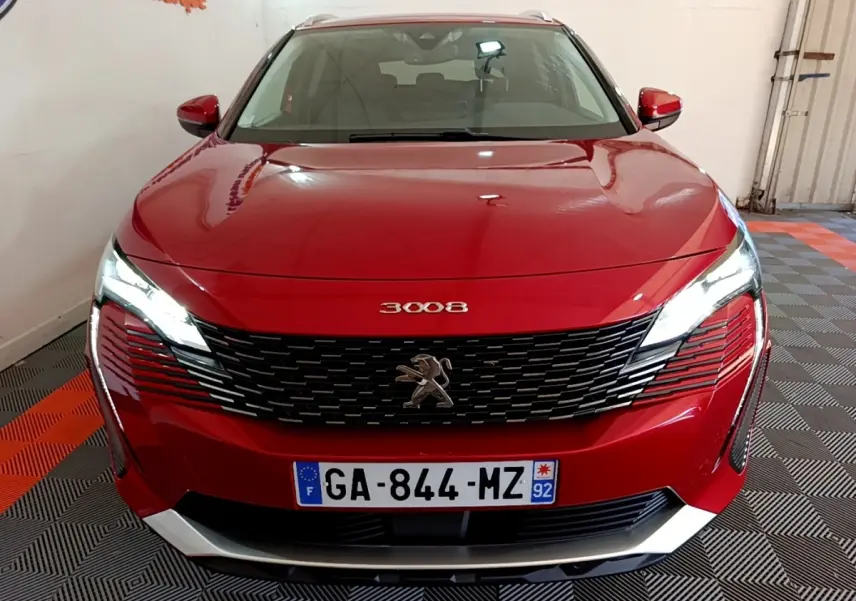 Vue avant d'un Peugeot 3008 hybride rechargeable rouge avec calandre noire et phares LED allumés dans un garage.