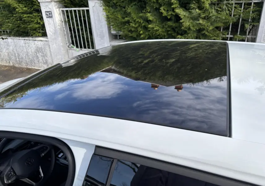 Toit panoramique noir sur une Volkswagen Golf blanche 2024, vue plongeante sur l'avant côté gauche avec intérieur visible.