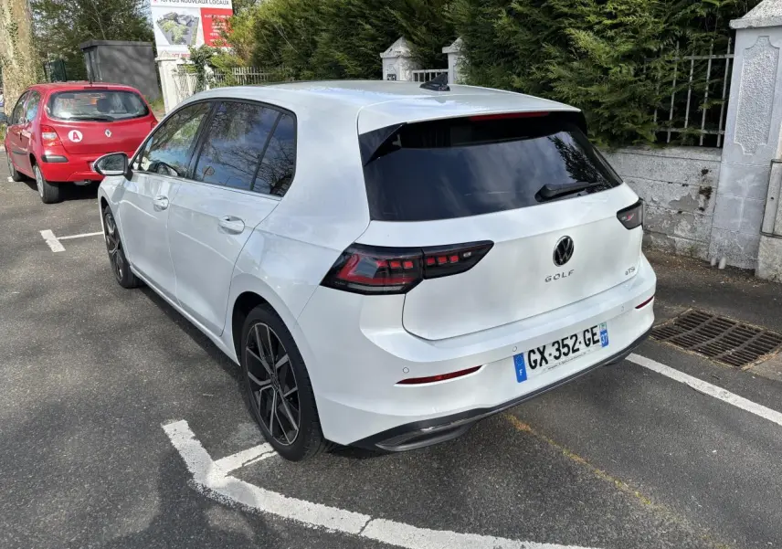 Vue 3/4 arrière droite d'une Volkswagen Golf blanche 2024 avec feux arrière LED et jantes noires en alliage.