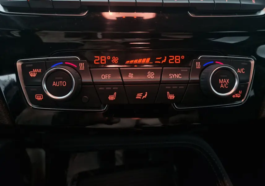 Détail du tableau de bord du BMW X2 gris clair, montrant la commande de climatisation digitale réglée à 28 degrés.