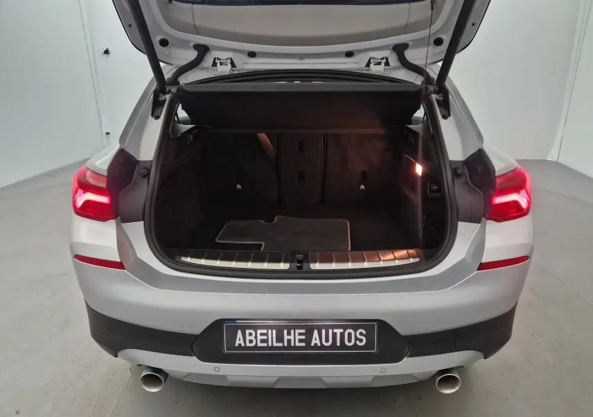 Vue arrière d’un BMW X2 gris clair métal avec coffre ouvert et feux arrière allumés dans un studio.