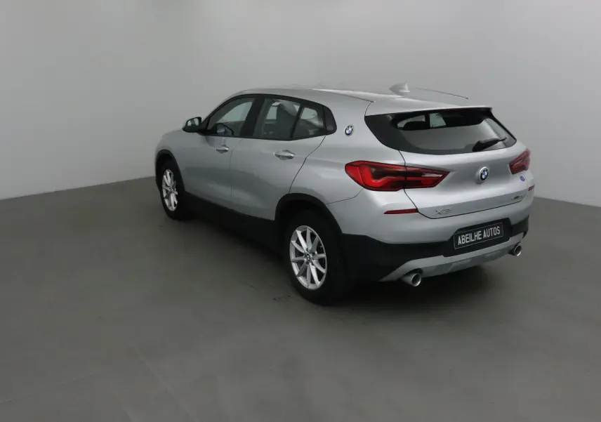 BMW X2 gris clair métal vue 3/4 arrière droit, avec feux arrière LED et double sortie d’échappement visible.