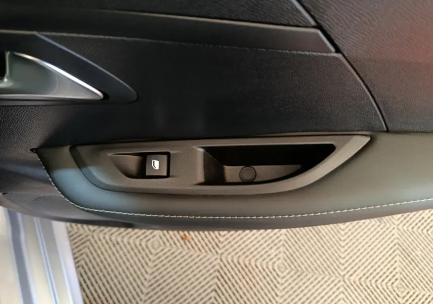 Détail de la commande de lève-vitre sur la porte intérieure côté conducteur d’une Peugeot 208 gris clair.