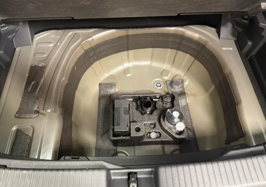 Coffre ouvert du Volkswagen T-Cross gris cendre 2025, vue plongeante sur le rangement sous plancher avec outils et compresseur.