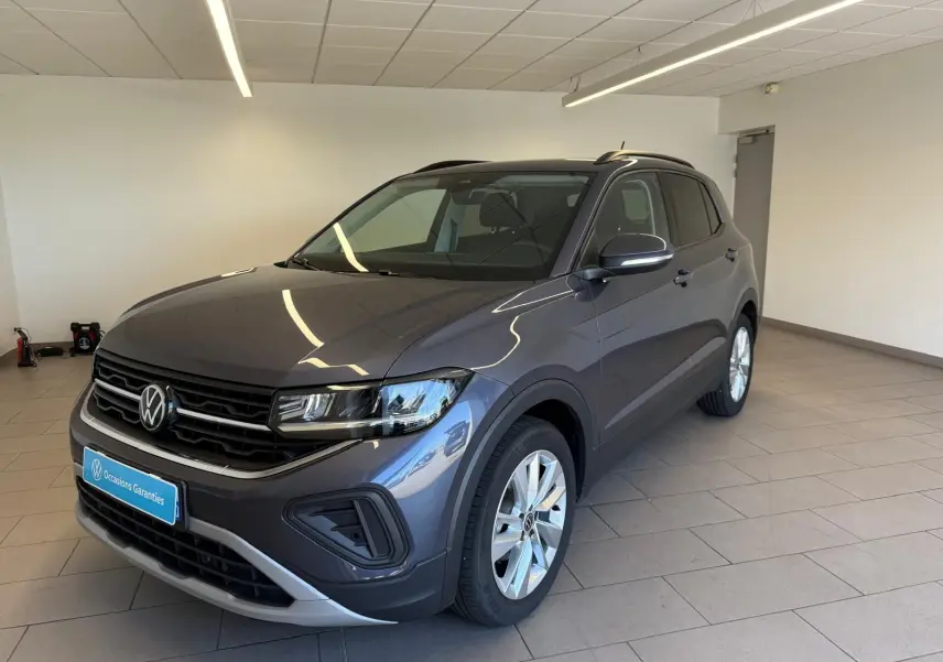 Volkswagen T-Cross gris cendre en 3/4 avant droit, avec calandre noire et jantes argentées, dans un showroom lumineux.