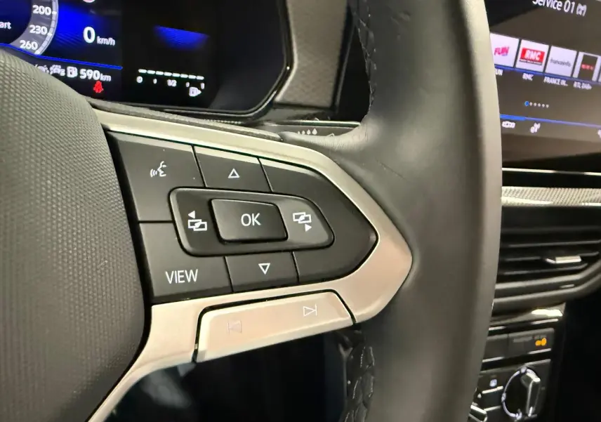 Gros plan sur le volant côté gauche du Volkswagen T-Cross gris cendre 2025, avec commandes multifonctions et tableau de bord numérique.