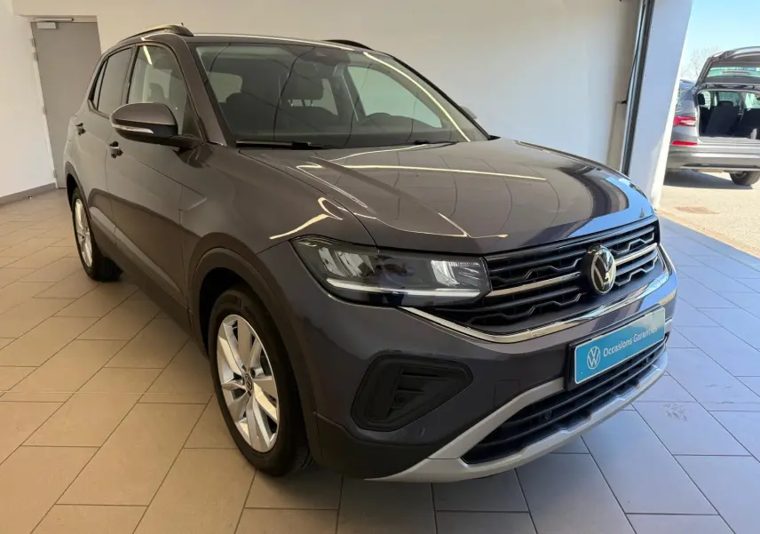 Volkswagen T-Cross 2025 gris cendre en 3/4 avant droit, avec calandre noire et détails chromés visibles en showroom.