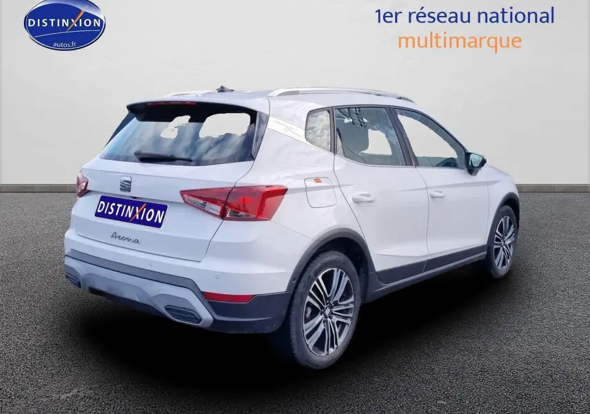 SEAT Arona blanc vue 3/4 arrière droit, avec jantes alu 17 pouces et barres de toit visibles.