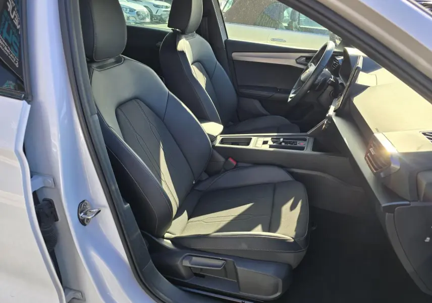 Vue intérieure côté conducteur d'une CUPRA Leon Sportstourer blanche Nevada, sièges noirs et tableau de bord moderne.