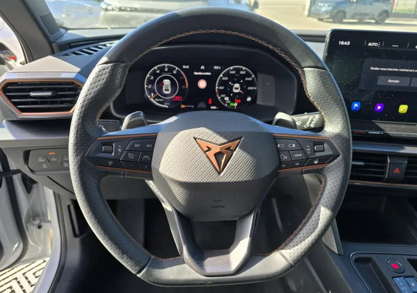 Volant Cupra perforé avec logo cuivre, tableau de bord digital et écran tactile dans l'habitacle d'une Leon Sportstourer blanche.