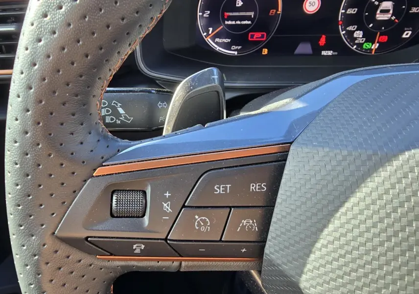 Gros plan sur les commandes du volant en cuir perforé du Cupra Leon Sportstourer blanc Nevada, avec combiné digital visible.