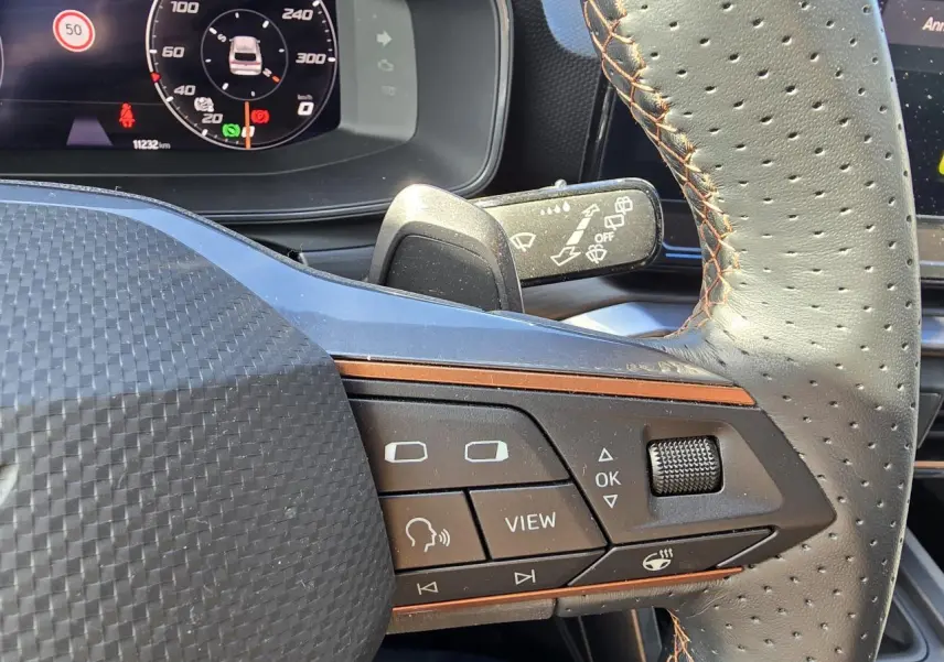 Gros plan sur les commandes du volant cuir perforé avec surpiqûres marron du CUPRA Leon Sportstourer blanc Nevada 2024.