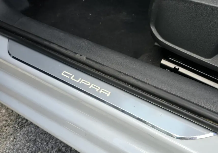 Gros plan sur la plaque de seuil de porte illuminée Cupra, sur fond de carrosserie blanc Nevada métallisé.