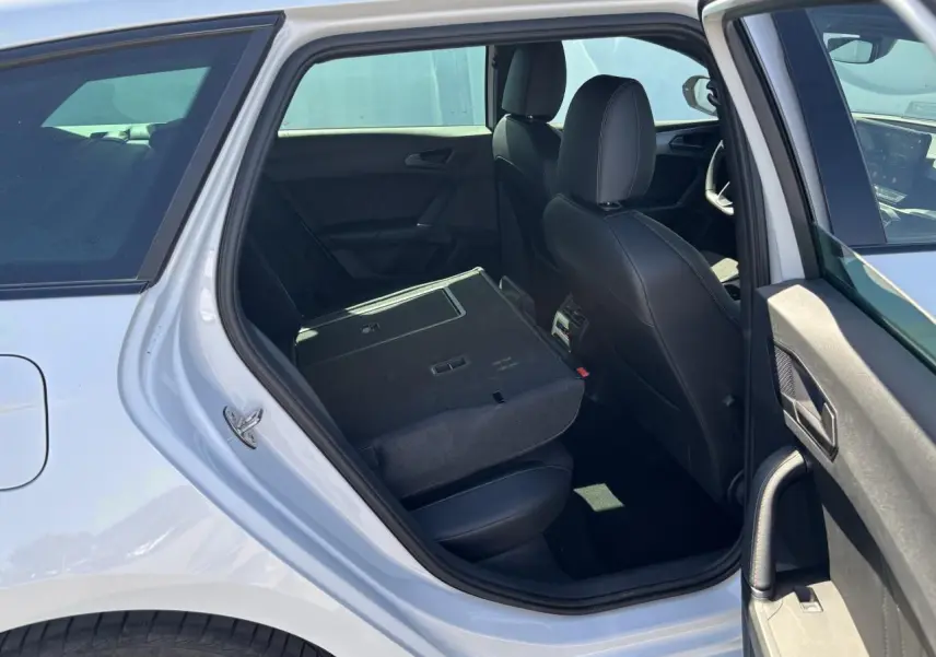 Vue intérieure côté gauche arrière de la CUPRA Leon Sportstourer blanche avec banquette rabattue et sièges noirs en cuir.