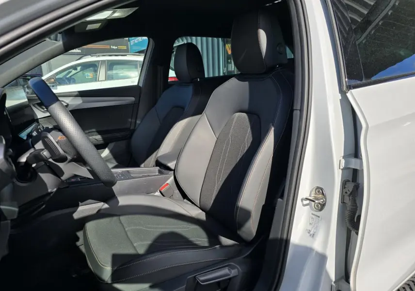 Vue intérieure côté conducteur d'une CUPRA Leon Sportstourer blanche Nevada, sièges sport en cuir et tissu noir.