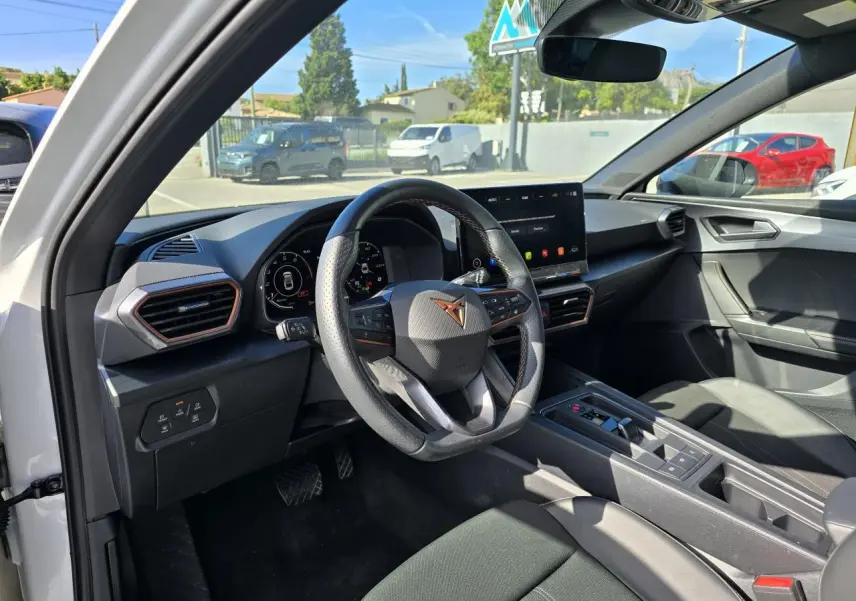 Vue intérieure côté conducteur du CUPRA Leon blanc Nevada, avec volant sport, écran tactile HD et tableau de bord digital.