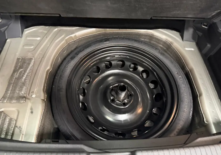 Gros plan sur la roue de secours compacte noire dans le coffre du Volkswagen T-Cross 2024 couleur Reflet d'Argent.