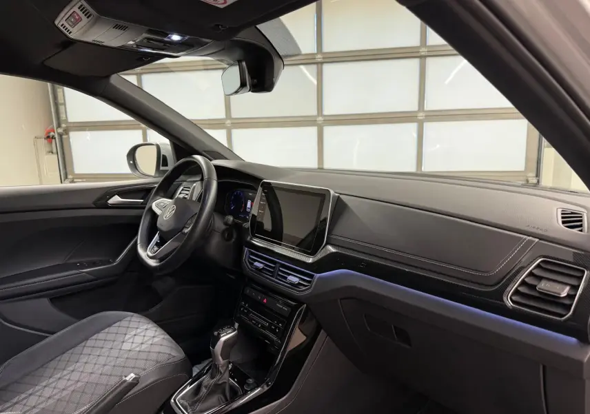 Vue intérieure côté conducteur du Volkswagen T-Cross 2024, tableau de bord noir avec écran tactile central et volant multifonction.
