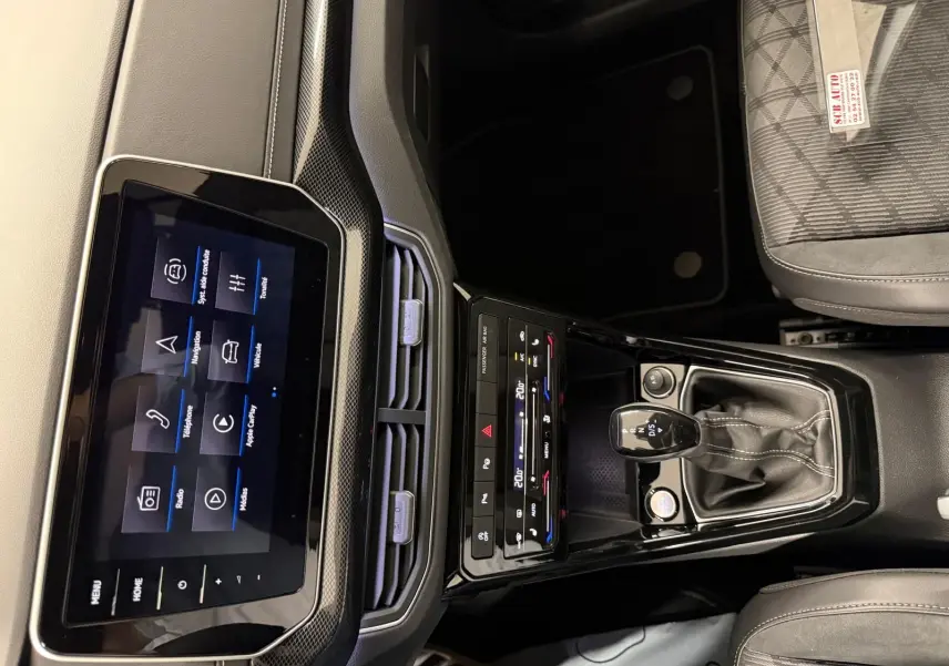 Vue intérieure centrée sur la console centrale et l'écran tactile du Volkswagen T-Cross 1.5 TSI R-Line, finition noire.