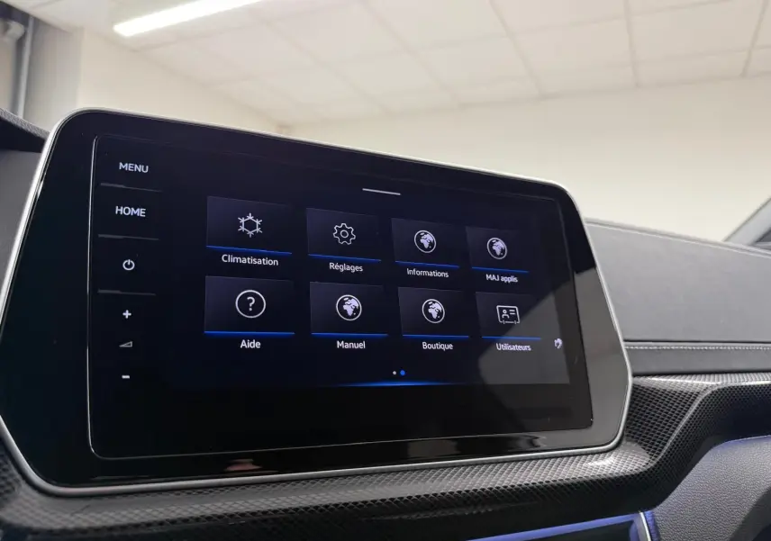 Écran tactile central du Volkswagen T-Cross 2024, affichant le menu des réglages, avec finition carbone et éclairage d'ambiance bleu.