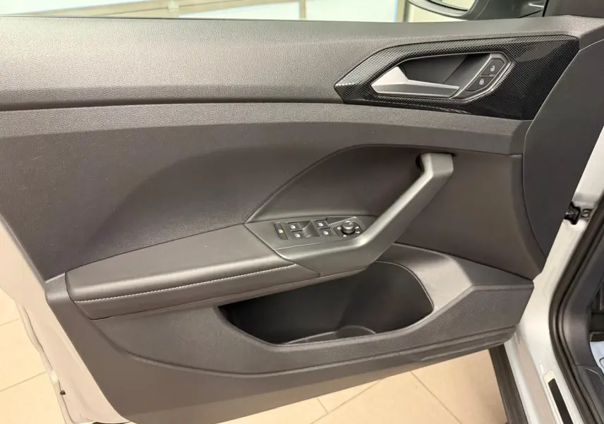 Vue intérieure de la porte avant gauche du Volkswagen T-Cross 2024 en Reflet d'Argent, avec commandes électriques et poignée intégrée.
