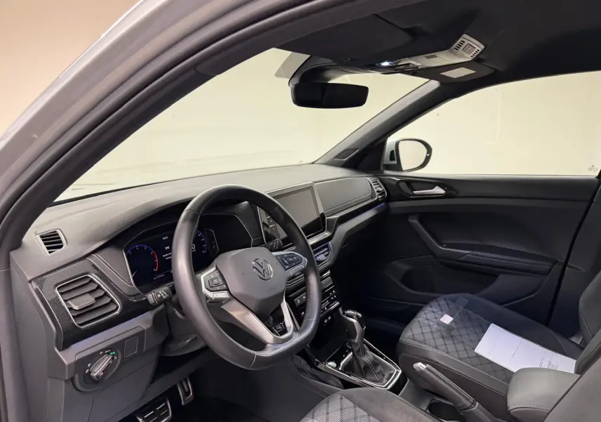 Vue intérieure côté conducteur du Volkswagen T-Cross 1.5 TSI R-Line 2024, tableau de bord et sièges noirs avec surpiqûres.