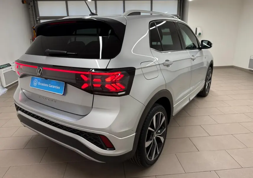 Vue 3/4 arrière droite du Volkswagen T-Cross 1.5 TSI R-Line 2024 en peinture métallisée Reflet d'Argent avec feux arrière LED allumés.