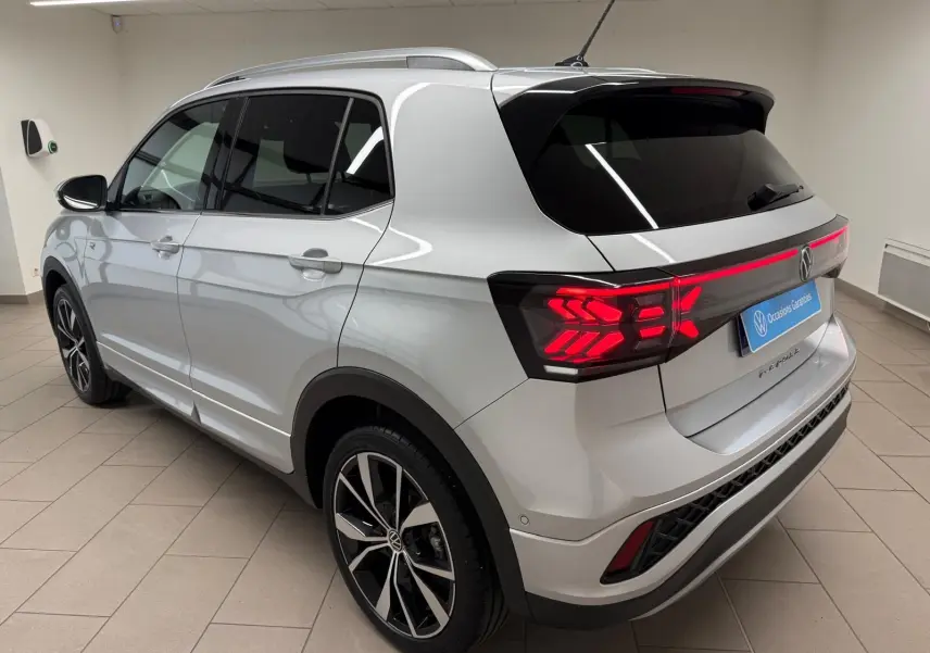 Vue 3/4 arrière droite du Volkswagen T-Cross 1.5 TSI R-Line argent métallisé avec feux arrière LED allumés et jantes alliage 18 pouces.
