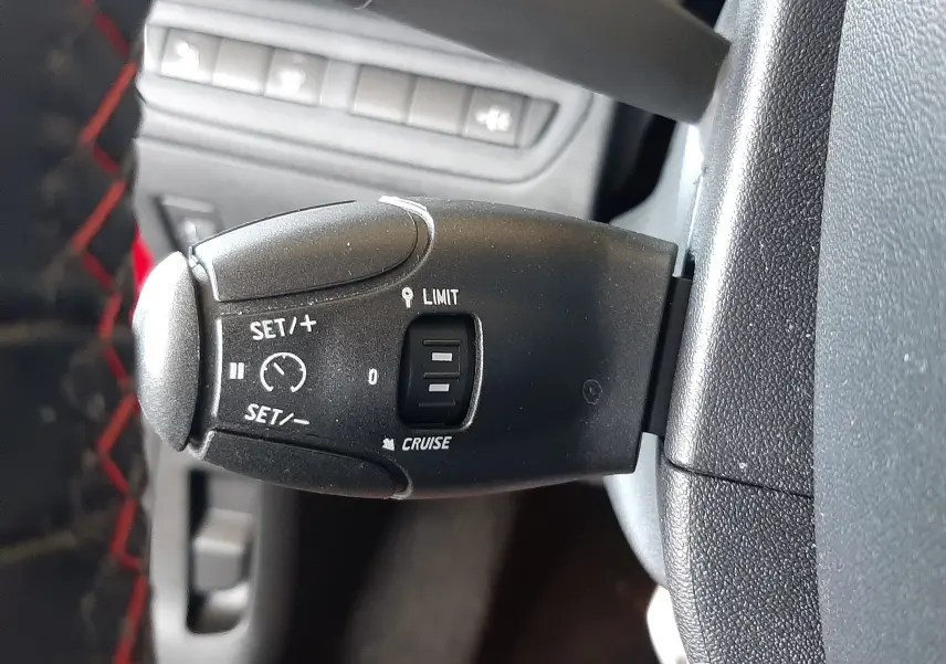 Gros plan sur la commande de régulateur de vitesse noire dans l'habitacle d'une Peugeot 2008 rouge Ultimate Metal.