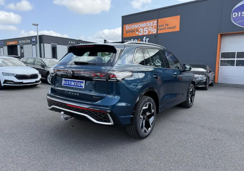 Vue 3/4 arrière droite d'un Volkswagen Tiguan 2024 bleu métallisé avec attelage et jantes R-Line noires.