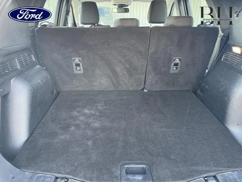 Vue intérieure du coffre spacieux du Ford Kuga 2023 avec banquette arrière en tissu noir relevée.