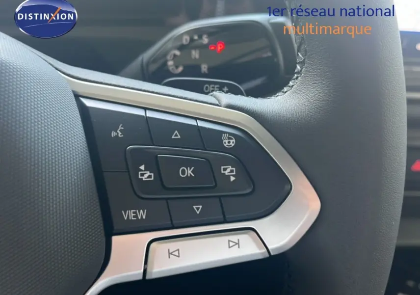 Gros plan sur les commandes au volant du Volkswagen Tiguan noir Grenadilla, mettant en valeur les boutons multifonctions et le tableau de bord flou.