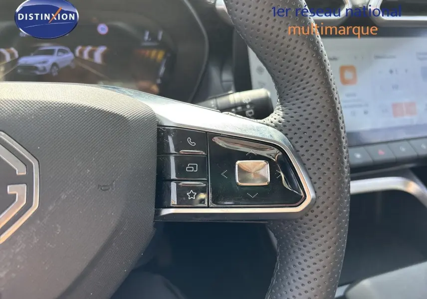Gros plan sur la partie droite du volant perforé noir du MG ZS 1.5L Hybrid+ 2025 avec commandes intégrées et écran tactile en arrière-plan.