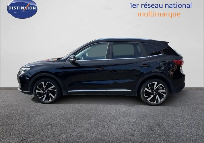 Vue de profil côté gauche d’un MG ZS 1.5L Hybrid+ 197ch Luxury en noir Pebble Black Metal avec jantes alliage bicolores.