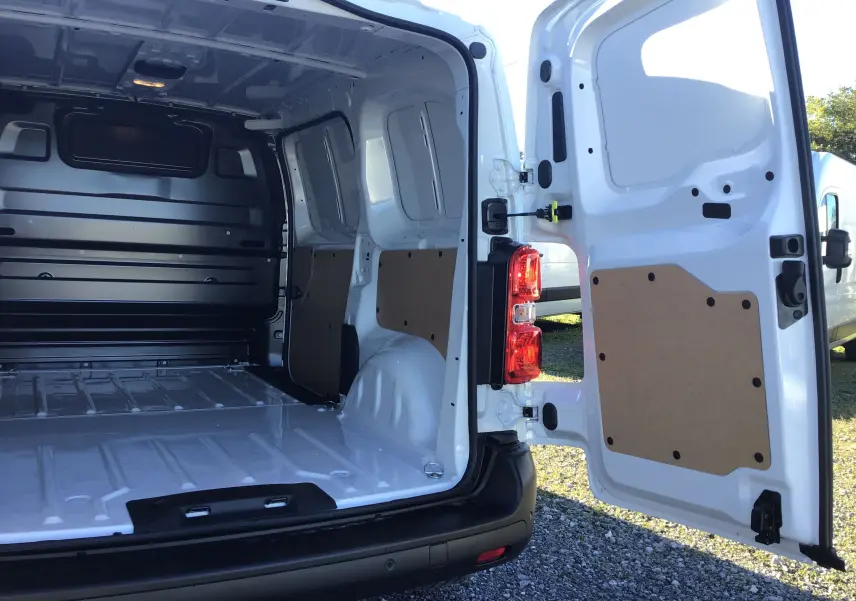 Vue arrière du fourgon blanc Peugeot Expert avec portes ouvertes montrant l'espace de chargement vide et les panneaux intérieurs.
