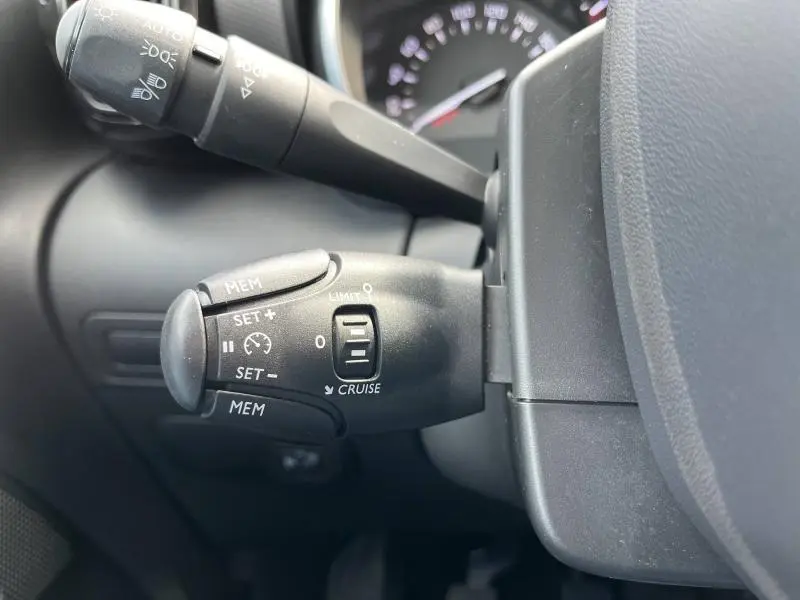 Gros plan sur la commande de régulateur de vitesse noire à gauche du volant dans l'habitacle gris du Citroën C3 Aircross 2020.