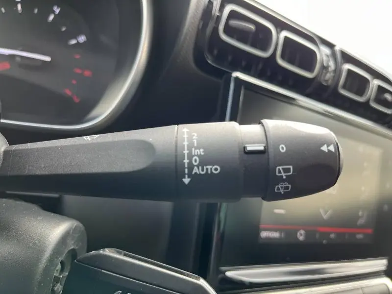 Gros plan sur la commande d'essuie-glace du tableau de bord d'une Citroën C3 Aircross gris acier, avec écran tactile en arrière-plan.