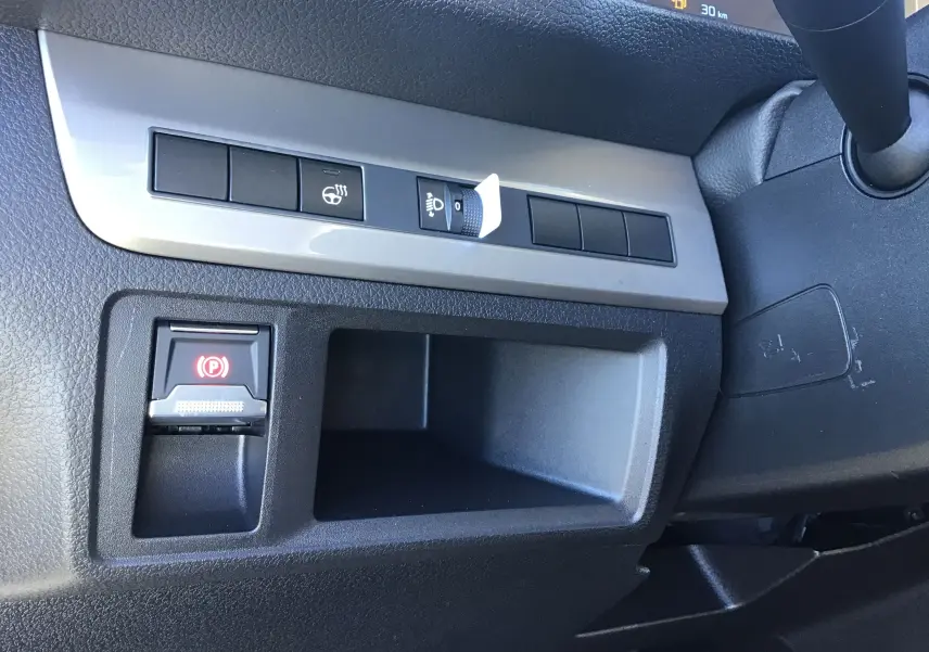 Gros plan sur la console côté gauche du Peugeot Expert Fourgon blanc 2024, montrant les commandes de frein à main électronique et réglage des phares.