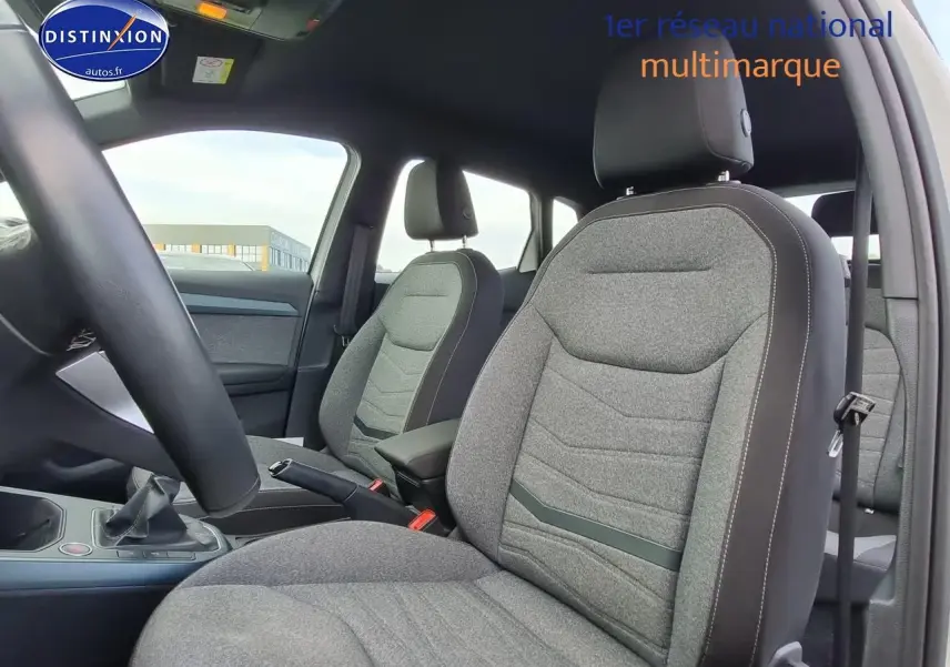 Intérieur du SEAT Arona 2023 essence, vue côté conducteur sur sièges gris tissu avec accoudoir central noir.