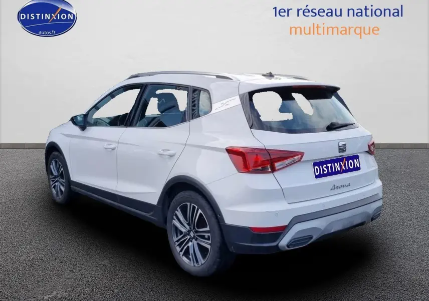 SEAT Arona blanc en 3/4 arrière droit, avec jantes alu 17 pouces et barres de toit visibles.