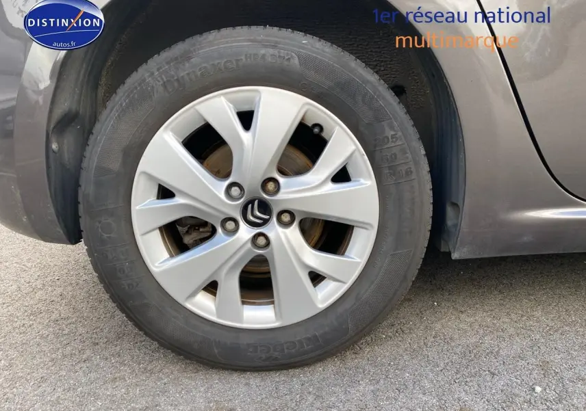 Gros plan sur la roue avant gauche d'une Citroën C4 Picasso gris métallisé avec jante alu et logo Citroën visible.