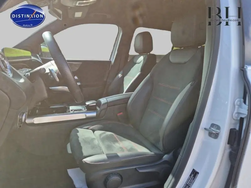 Intérieur côté conducteur du Mercedes GLB blanc polaire 2023, sièges sport noirs avec surpiqûres rouges et volant cuir.