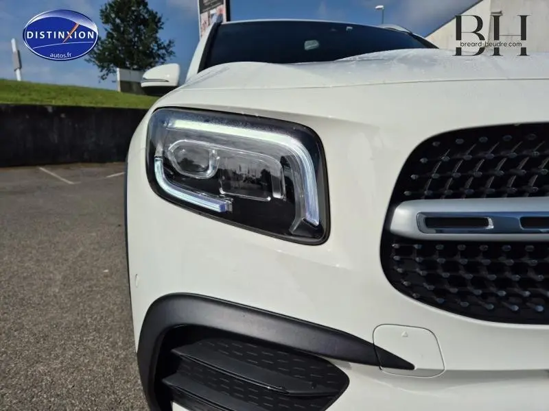 Gros plan sur le phare avant gauche et la calandre noire du Mercedes GLB 200 d blanc polaire AMG Line 2023