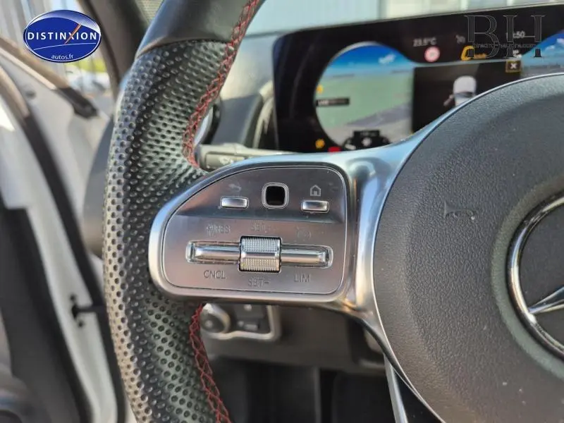 Gros plan sur les commandes au volant côté gauche d'un Mercedes GLB blanc polaire avec affichage numérique en arrière-plan.
