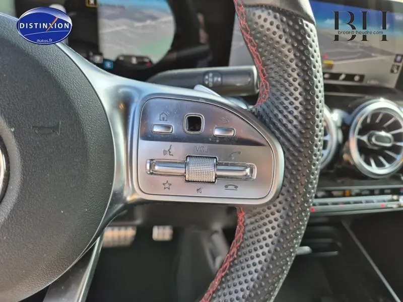 Gros plan sur la partie gauche du volant sport perforé noir avec surpiqûres rouges du Mercedes GLB blanc polaire 2023.