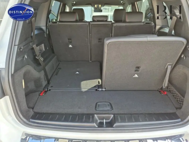 Vue arrière du coffre du Mercedes GLB blanc polaire avec sièges arrière partiellement rabattus et troisième rangée visible.