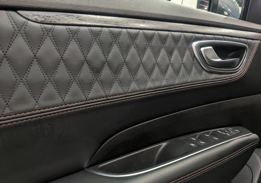Gros plan sur la garniture en cuir noir matelassé avec surpiqûres orange de la porte côté gauche du Renault Talisman Estate.