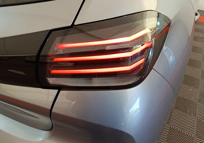 Gros plan sur le feu arrière droit allumé d’une Peugeot 208 gris clair, soulignant les lignes LED distinctives.