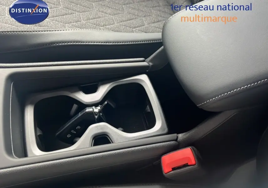 Gros plan intérieur sur le porte-gobelets central avec clé VW, sellerie noire et accoudoir en cuir cousu.