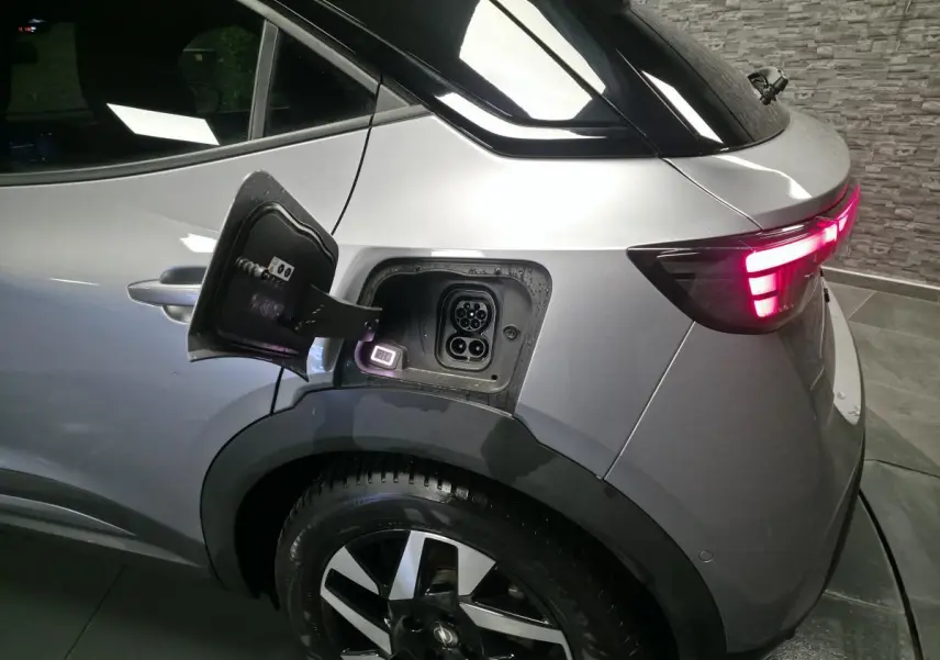 Vue arrière côté gauche d’un Opel Mokka-e gris avec trappe de recharge ouverte et feux arrière LED allumés.